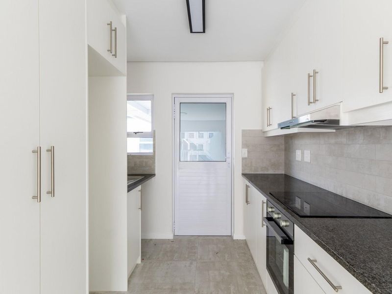 A modern, empty kitchen featuring white cabinetry, dark stone countertops, integrated oven and hob, and tiled finishes, ready for personalization.