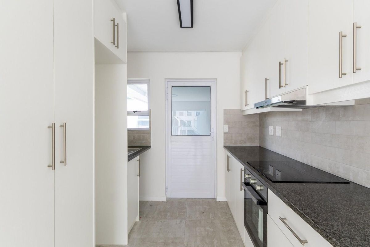 A modern, empty kitchen featuring white cabinetry, dark stone countertops, integrated oven and hob, and tiled finishes, ready for personalization.