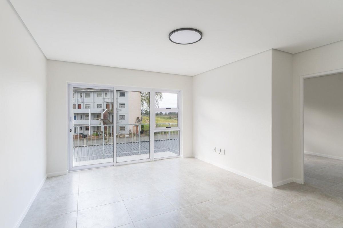 A bright, empty living room featuring neutral tiled flooring, a modern flush mount ceiling light, and large sliding glass doors leading to a balcony.