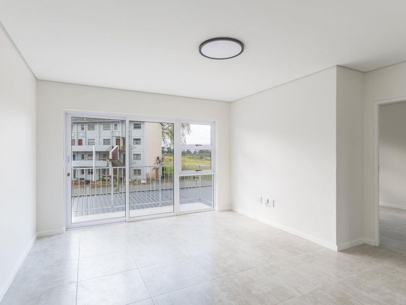 A bright, empty living room featuring neutral tiled flooring, a modern flush mount ceiling light, and large sliding glass doors leading to a balcony.