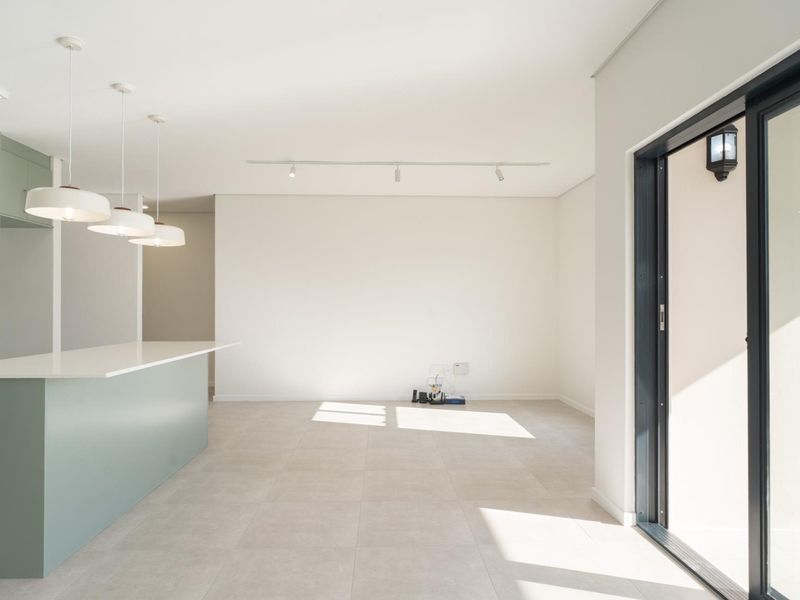 Modern open-plan living and kitchen area featuring a central island, contemporary pendant lighting, and large sliding glass doors leading to the garden.