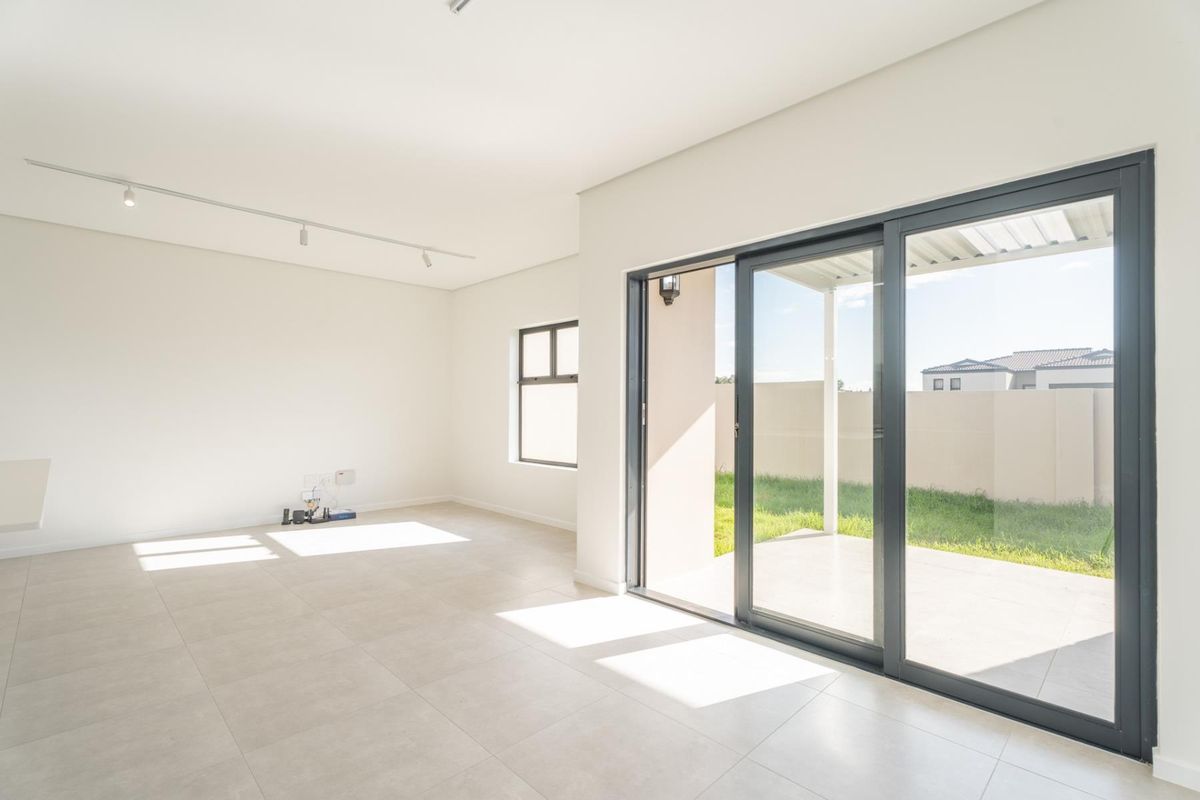 A bright, open-plan living area featuring neutral tiled flooring, modern track lighting, and large sliding glass doors providing direct access to the rear patio.