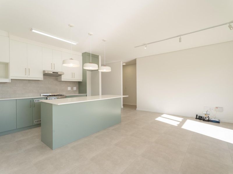 Modern open-plan kitchen and living area featuring a central island, contemporary cabinetry, stone countertops, and neutral tiled flooring throughout.