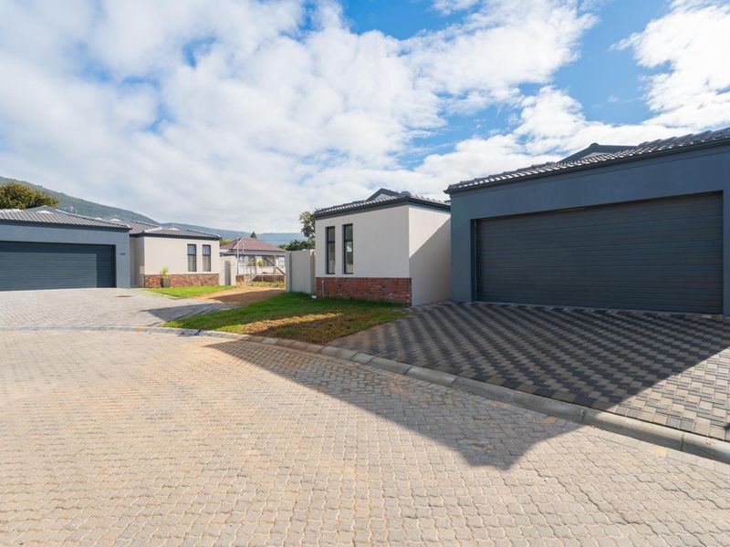 A street-level view of modern residential properties featuring paved driveways, double garages, and contemporary brick and render facades.