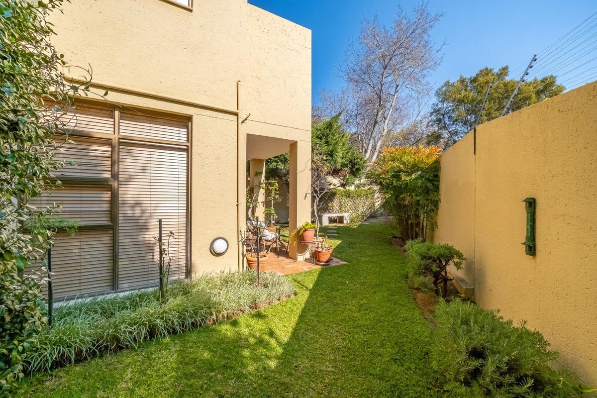 A private rear garden featuring a covered patio area, manicured lawn, and secure boundary walls with electric fencing.