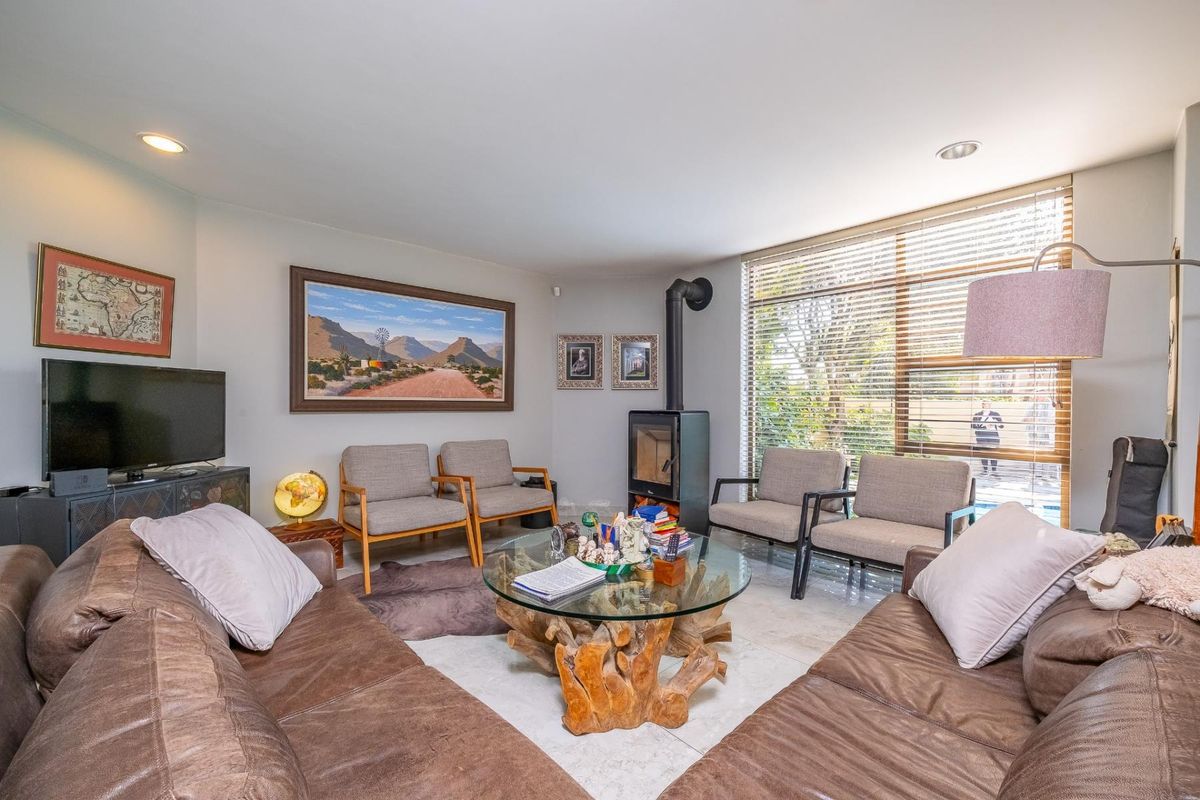 A comfortable living room featuring a modern freestanding fireplace, large windows with blinds, and neutral tiled flooring.