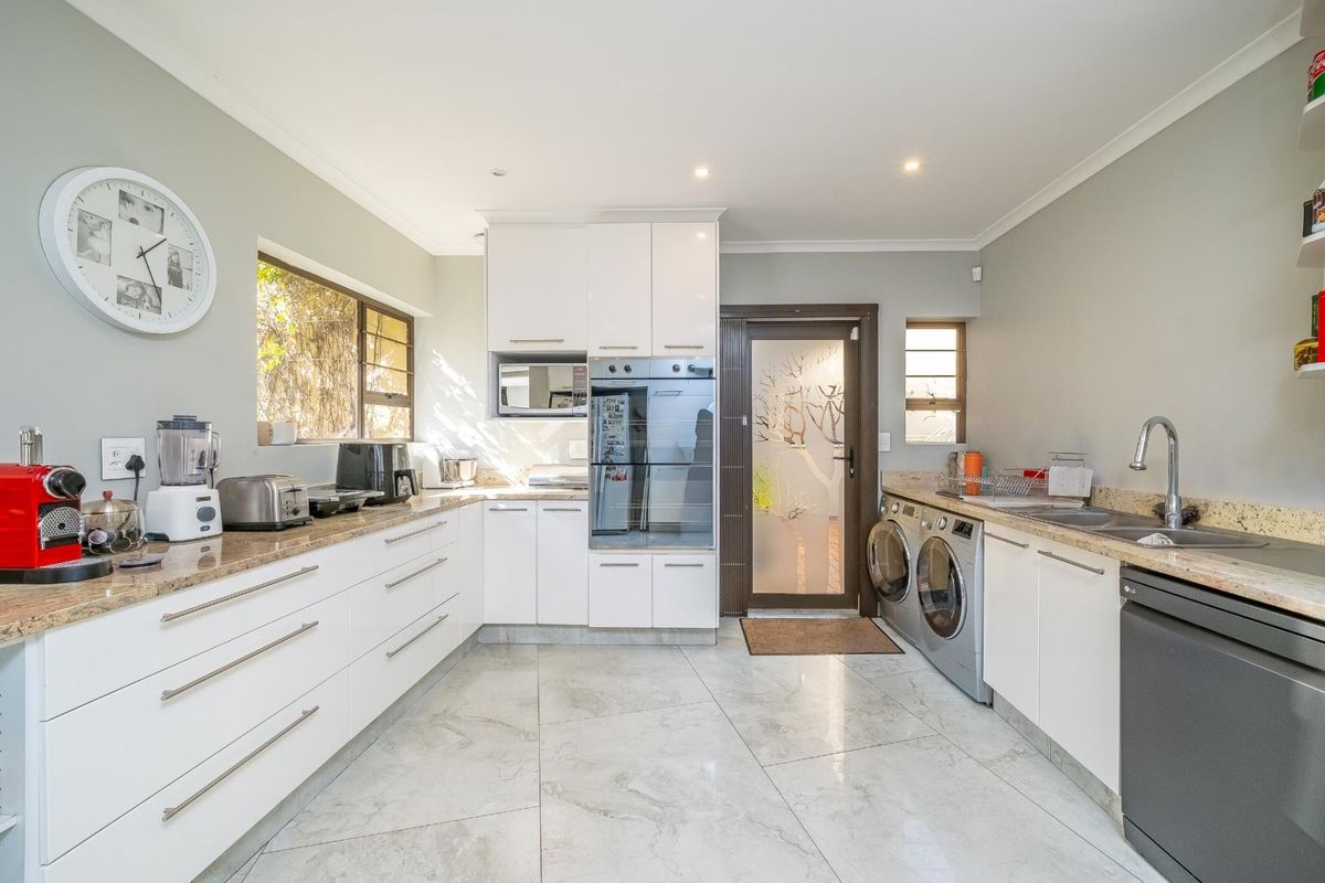Modern kitchen featuring white cabinetry, granite countertops, built-in oven and microwave, tiled flooring, and integrated laundry appliances with direct access to the exterior.