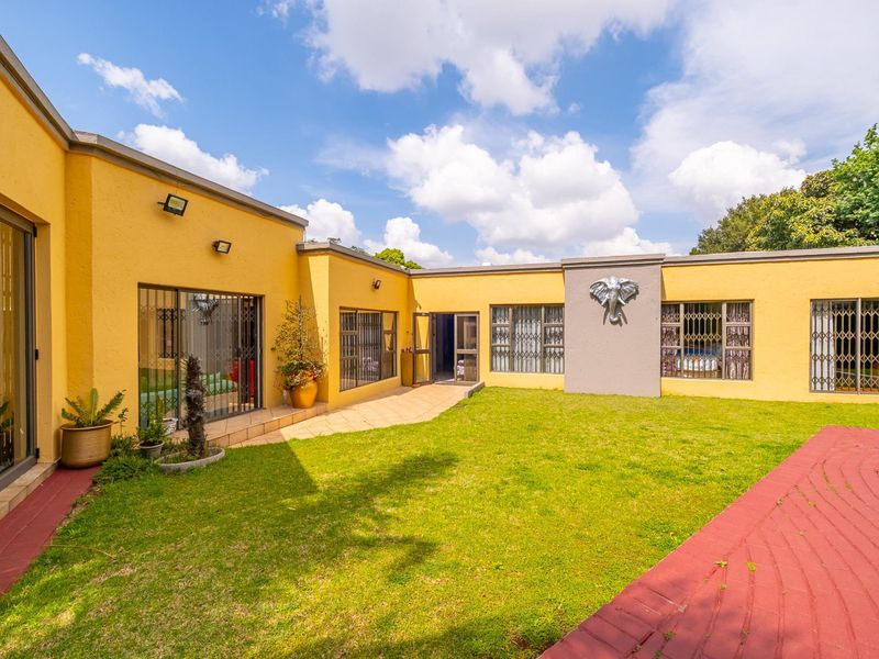 A well-maintained rear courtyard featuring a central lawn, paved pathways, and secure sliding door access to the main house structure.