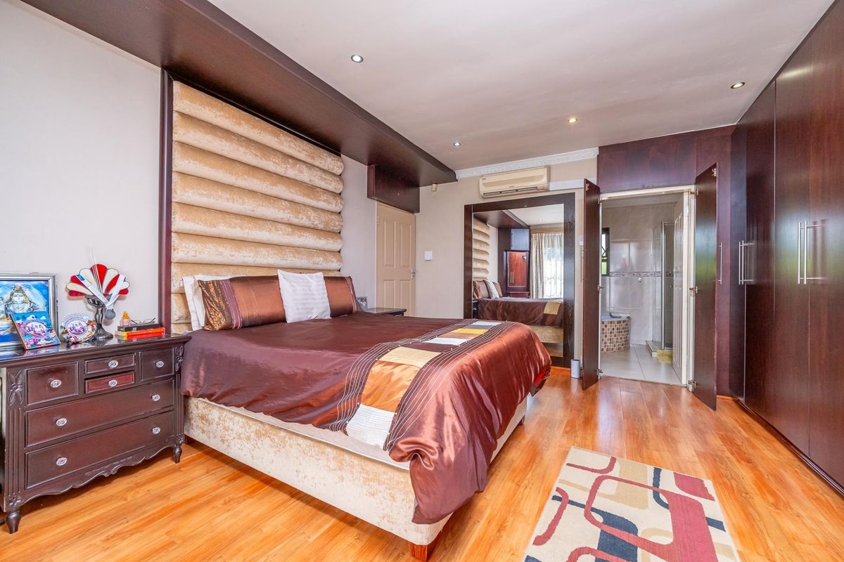 Spacious bedroom featuring laminate flooring, extensive built-in cabinetry, an integrated air conditioning unit, and direct access to an en-suite bathroom.