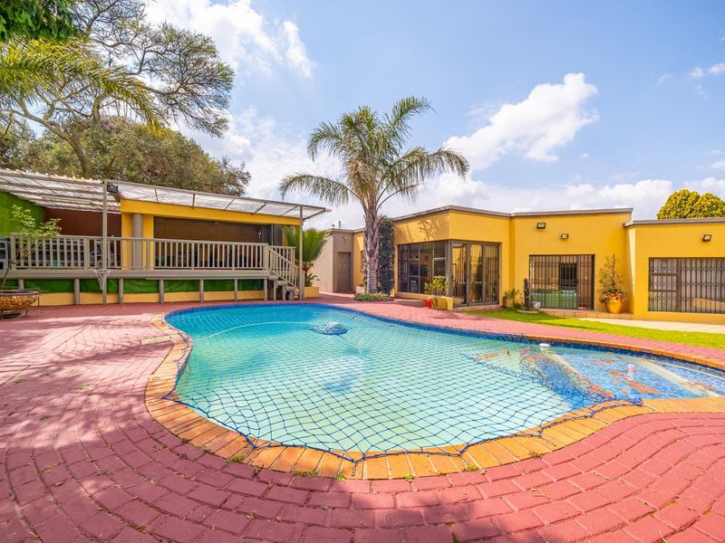 Outdoor pool area featuring a swimming pool with safety net, raised wooden deck, covered patio, and paved surround.