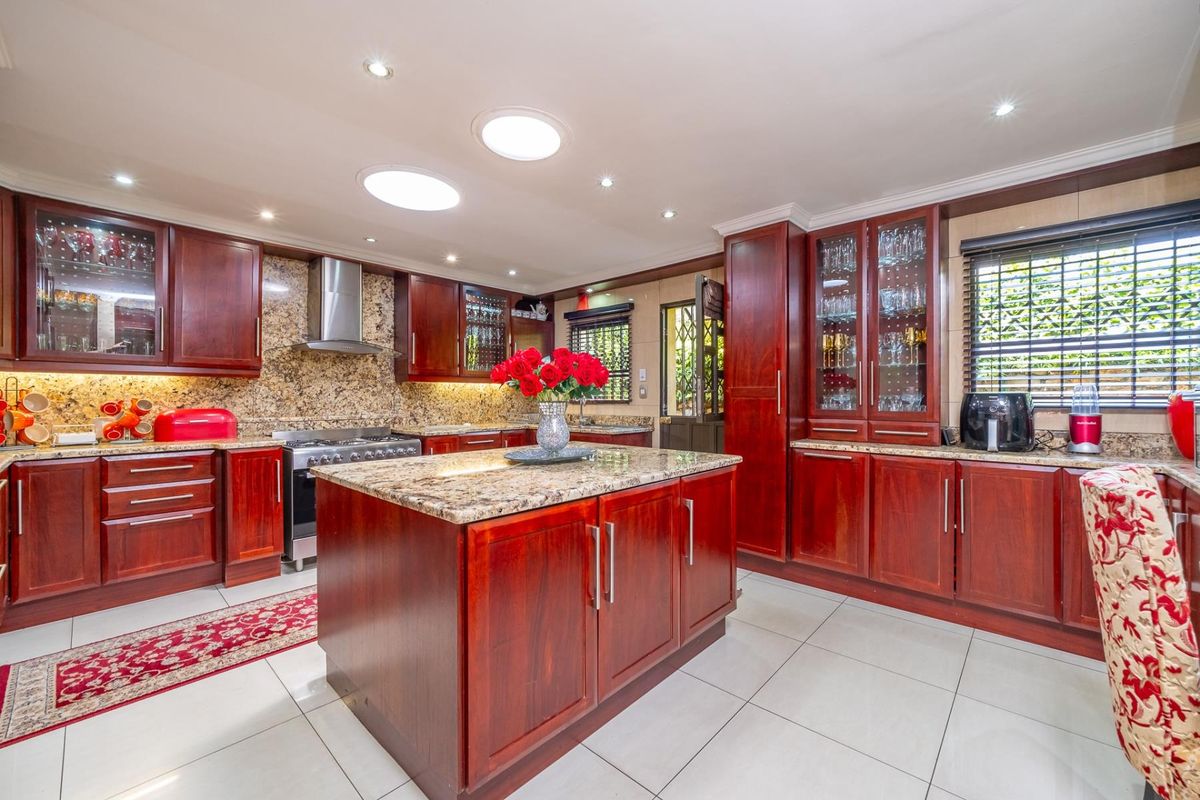 A well-appointed kitchen featuring rich cherry wood cabinetry, granite countertops, a central island, and modern stainless steel appliances under recessed lighting.