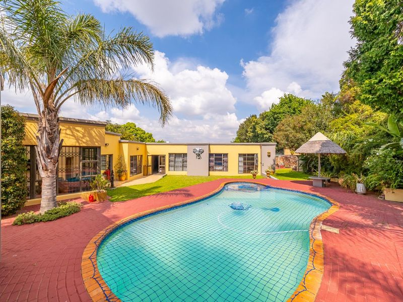 Spacious outdoor entertainment area featuring a swimming pool, brick paved surround, and a thatched umbrella set within a landscaped garden.