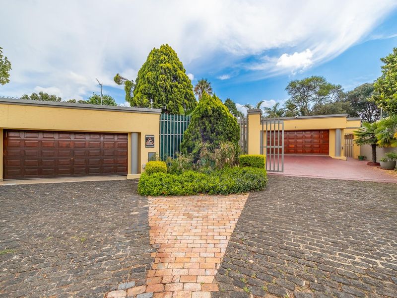 Front elevation of the property featuring a paved driveway, double and single garages, and secure perimeter walling with gated access.