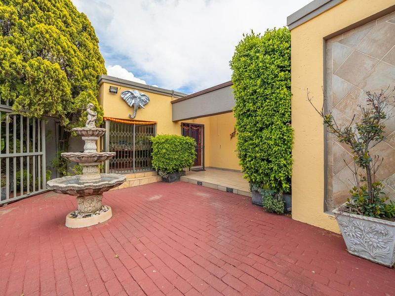A paved outdoor patio area featuring a decorative fountain, security gates, and tiled wall accents, providing a private entrance space.