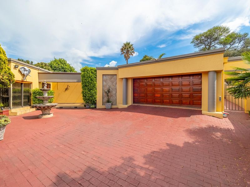 Front exterior view featuring a paved driveway, double garage, and decorative stone fountain in a well-maintained courtyard setting.