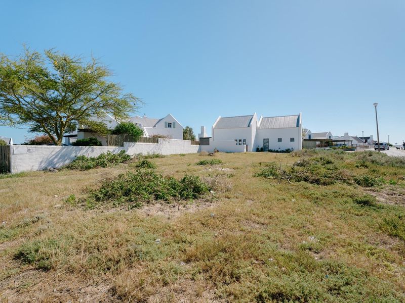 A vacant residential plot featuring a boundary wall and mature tree, situated in a developed coastal neighborhood.