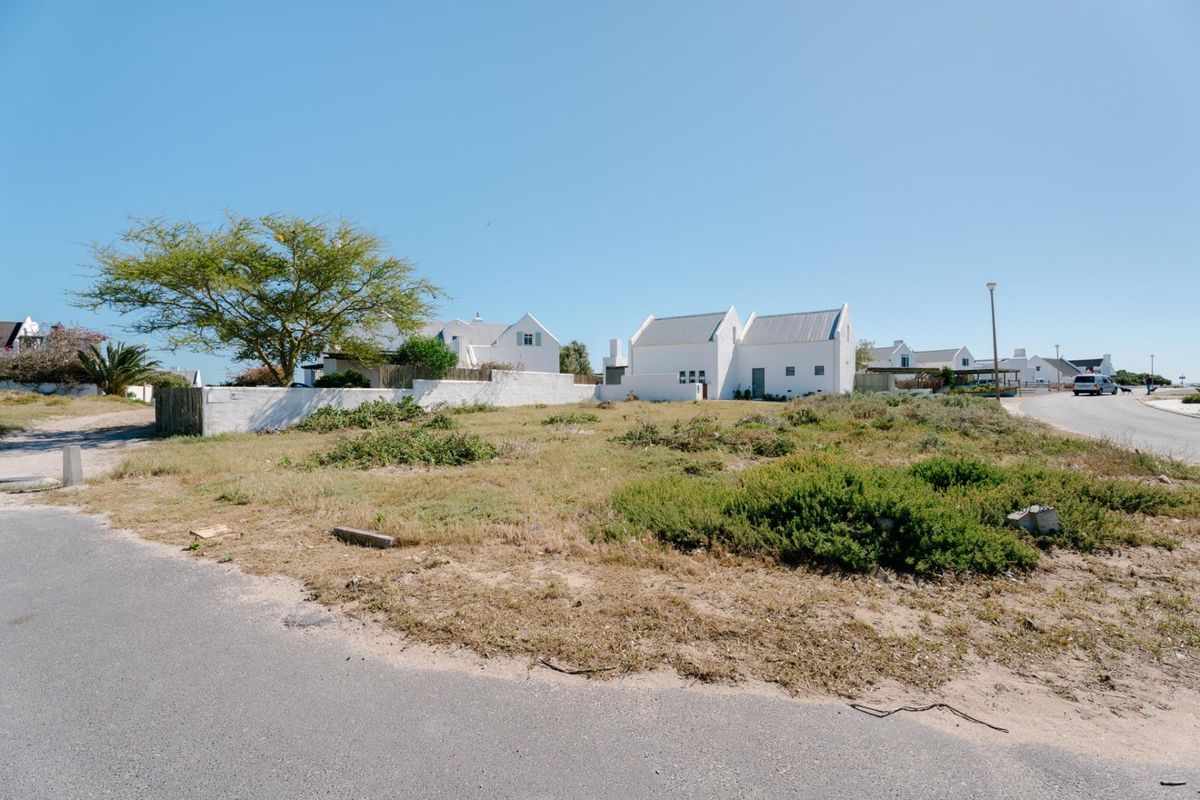 A vacant residential plot situated on a corner, featuring natural vegetation and boundary walling, with direct access to a paved street.