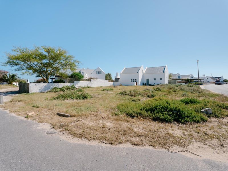 A vacant residential plot situated on a corner, featuring natural vegetation and boundary walling, with direct access to a paved street.