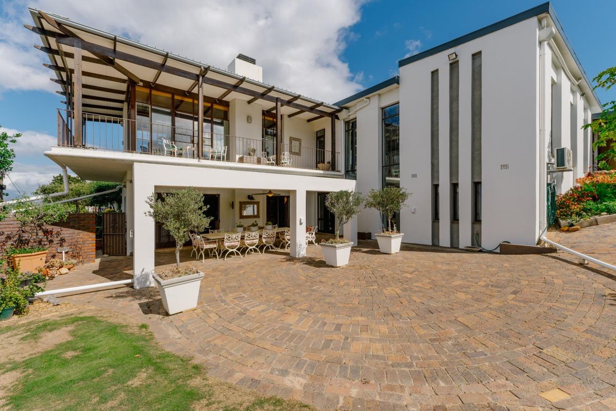 Spacious rear exterior featuring a paved courtyard, a covered ground-floor patio, and an expansive upper-level balcony with timber pergola detailing.
