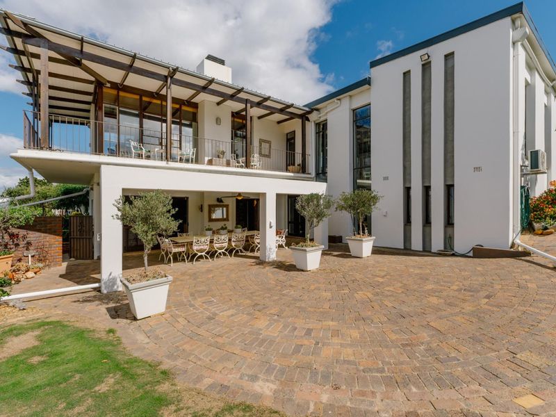 Spacious rear exterior featuring a paved courtyard, a covered ground-floor patio, and an expansive upper-level balcony with timber pergola detailing.