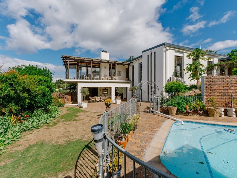Rear exterior view featuring a swimming pool, paved patio area, covered balcony, and landscaped garden space.
