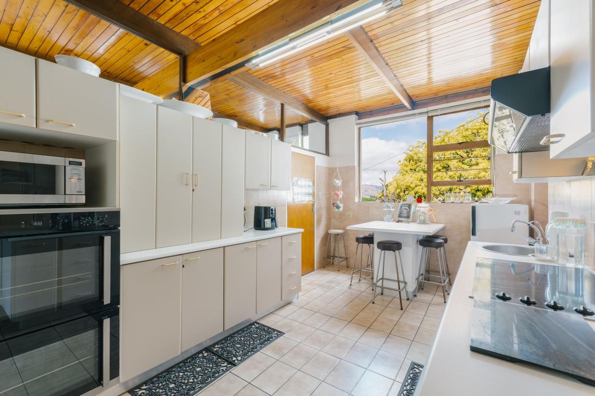 A functional kitchen featuring built-in cabinetry, integrated appliances, tiled flooring, and a distinctive timber-paneled ceiling with natural light.