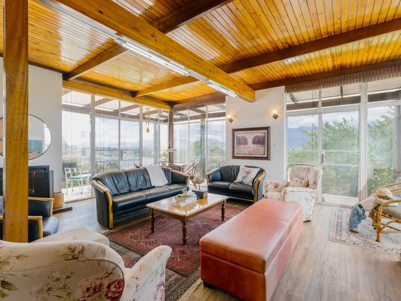 Spacious living room featuring a vaulted timber-clad ceiling, exposed beams, and extensive floor-to-ceiling glass windows offering abundant natural light and scenic views.