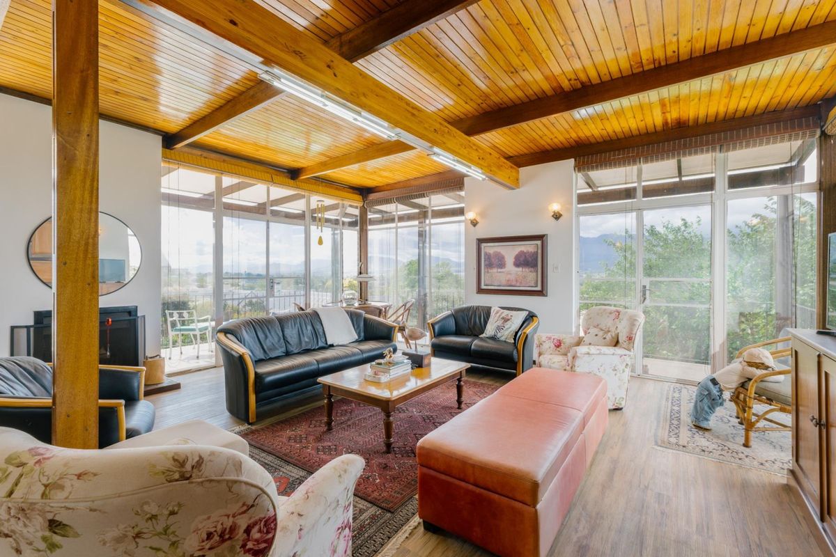 Spacious living room featuring a vaulted timber-clad ceiling, exposed beams, and extensive floor-to-ceiling glass windows offering abundant natural light and scenic views.