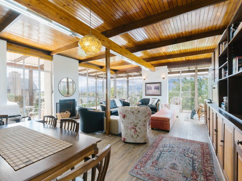 Spacious open-plan living and dining area featuring a vaulted timber ceiling, exposed beams, built-in fireplace, and extensive glass doors offering natural light and views.