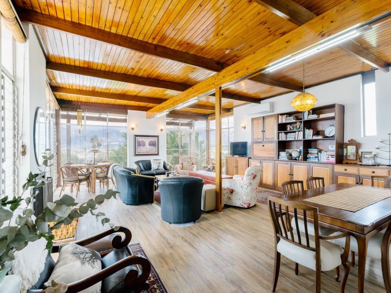 Spacious open-plan living and dining area featuring exposed timber ceiling beams, extensive built-in cabinetry, and large windows offering natural light and scenic views.