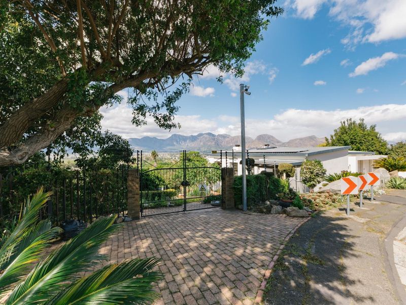 Front entrance view featuring a paved driveway, secure metal gate, and mountain views in the background.