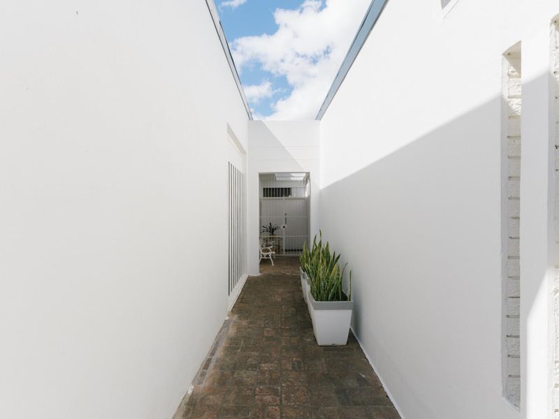 A bright, open-air outdoor corridor featuring brick paving and a secure metal gate entrance.