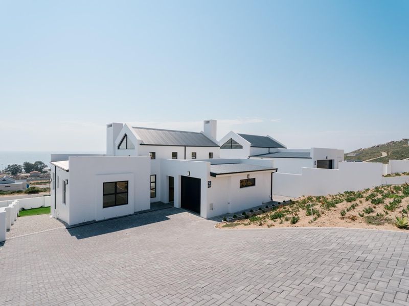 Modern coastal residence featuring a clean white facade, dark metal roofing, and a spacious paved driveway with ocean views.