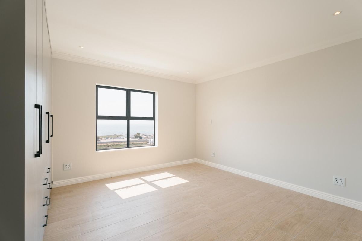 A bright, modern, and empty bedroom featuring neutral tiled flooring, built-in cupboards, and a window with a view.