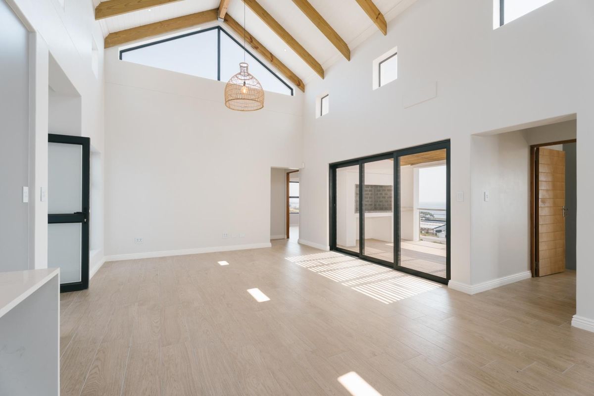 Spacious living area featuring a high vaulted ceiling with exposed timber beams, large sliding glass doors, and modern tiled flooring.