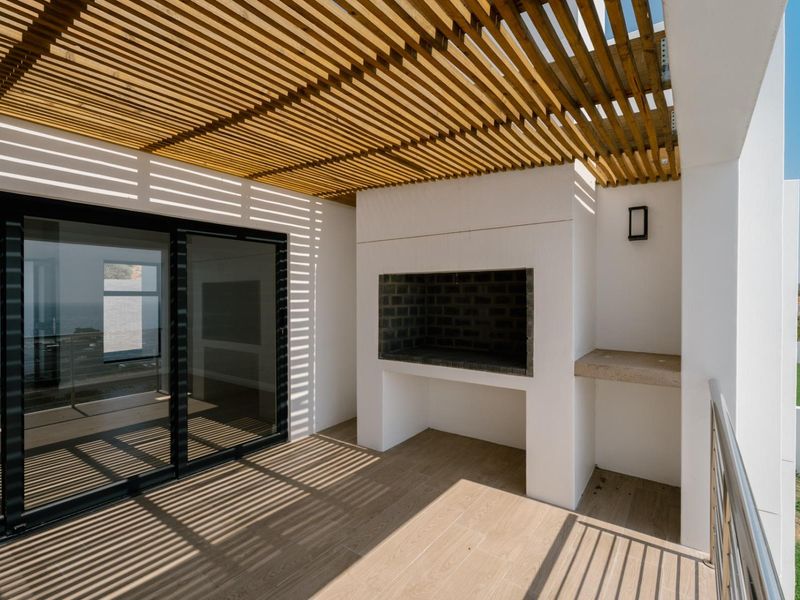 A modern covered patio featuring a wooden pergola, built-in braai, stone prep counter, and sliding glass doors leading to the interior.