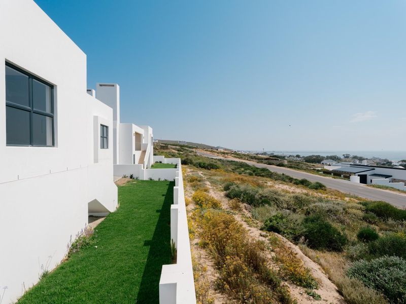 A modern white exterior facade featuring clean lines, framed windows, and a well-maintained lawn overlooking a coastal landscape.