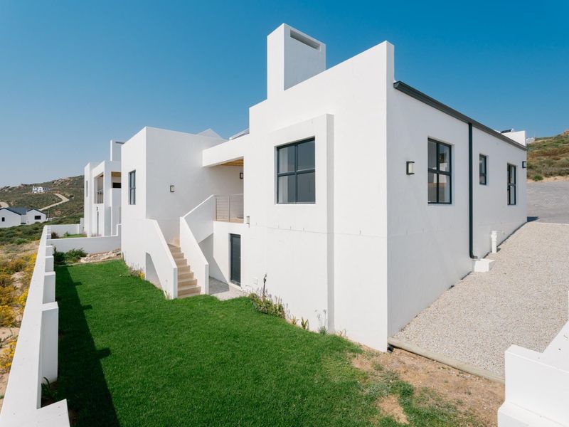 Rear view of a modern white multi-level house featuring clean architectural lines, an external staircase, a balcony, and a landscaped lawn area.