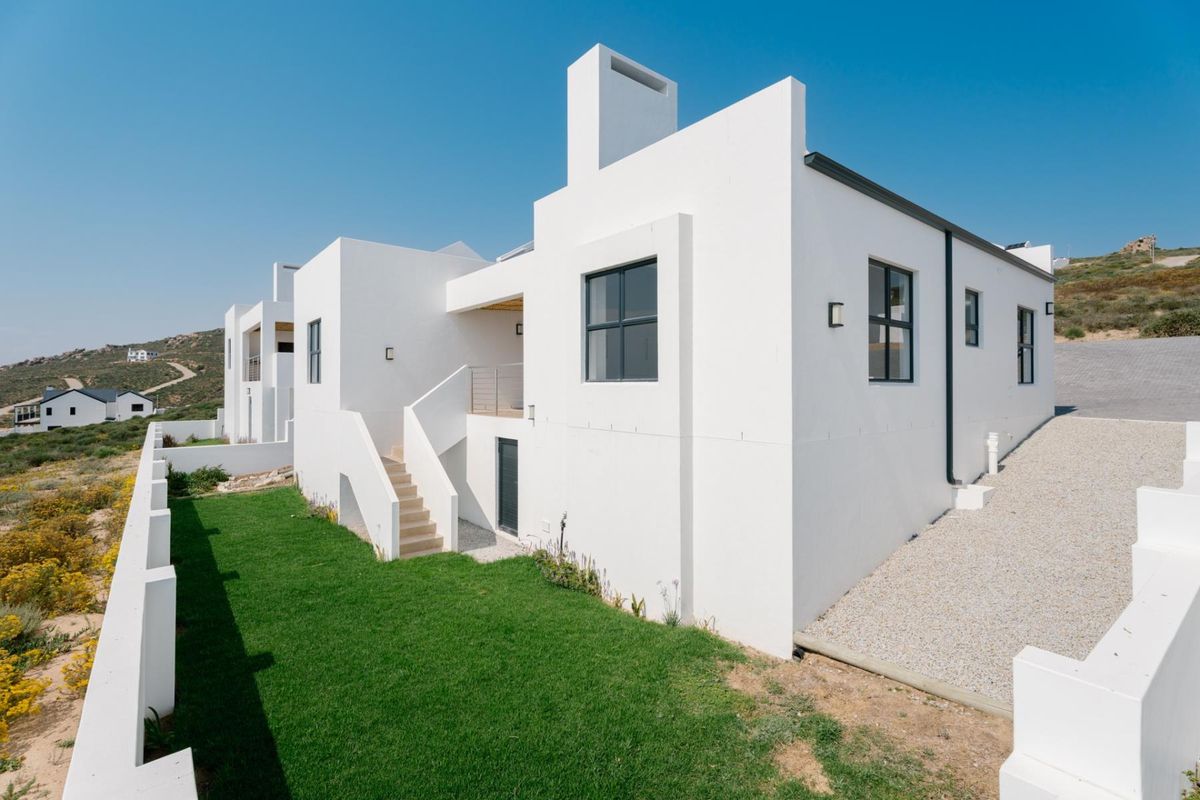 Rear view of a modern white multi-level house featuring clean architectural lines, an external staircase, a balcony, and a landscaped lawn area.