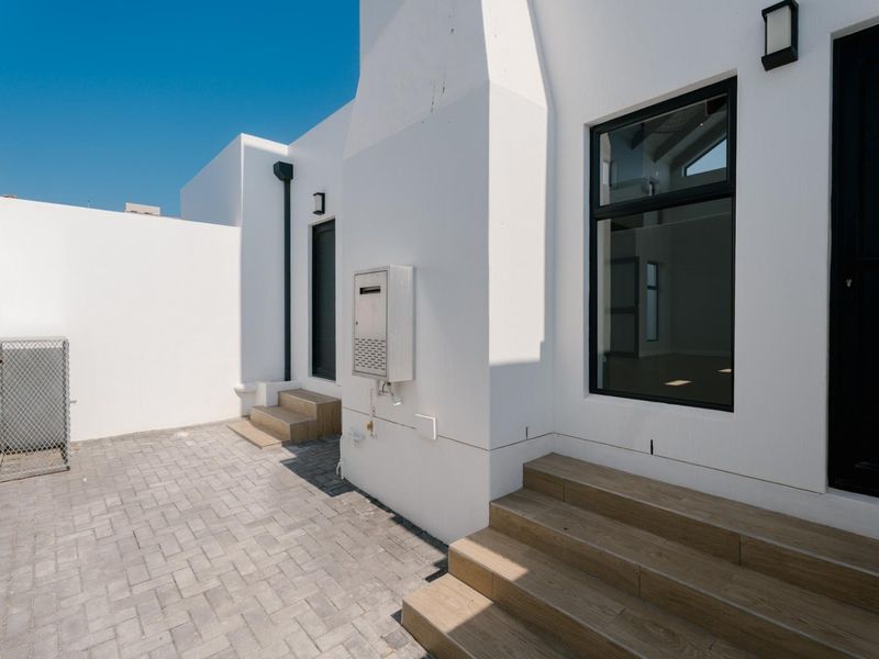 A clean, modern rear courtyard featuring paved flooring, tiled steps, and contemporary white exterior finishes with black window frames.