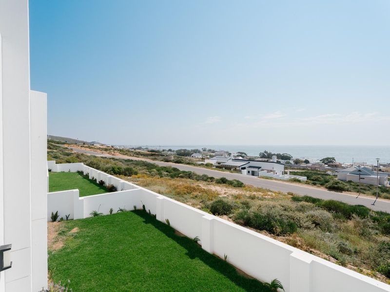 Elevated coastal view overlooking a manicured lawn, boundary walls, and the surrounding landscape towards the ocean.