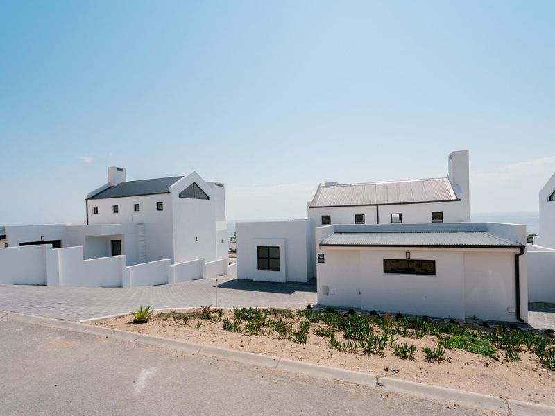 Modern white residential complex featuring clean architectural lines, metal roofing, and paved driveway access.