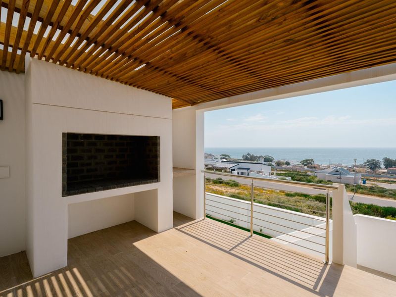 A modern covered balcony featuring a built-in braai, wooden pergola ceiling, and stainless steel balustrade, offering expansive coastal views.