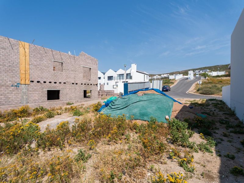 A view of a residential plot under construction featuring exposed concrete block walls and unimproved land in a coastal estate setting.