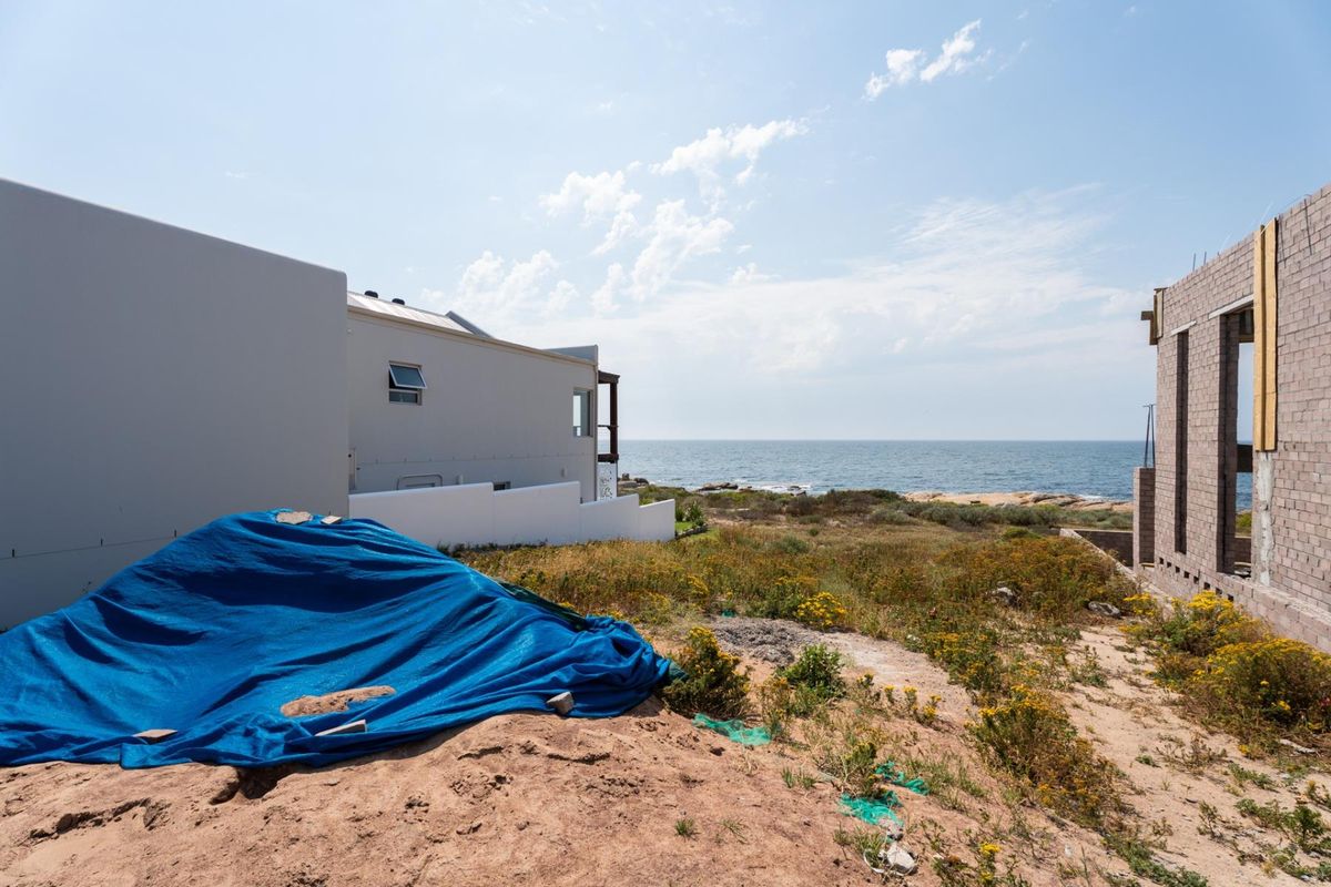 A view of a vacant residential plot featuring coastal scenery, adjacent modern housing, and ongoing construction work on the neighboring property.