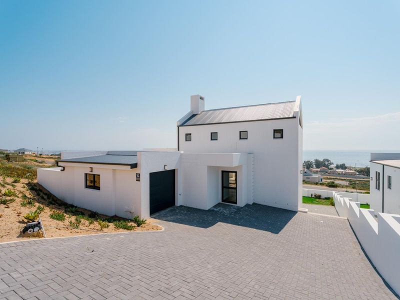 Modern white house exterior featuring a paved driveway, integrated garage, and clean architectural lines with a coastal view.