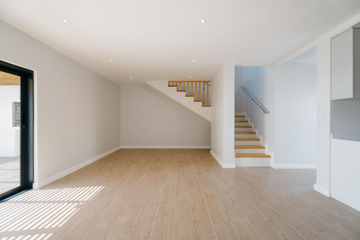 A bright, open-plan living area featuring modern timber-look tile flooring, recessed lighting, and a staircase with timber treads and a sleek metal handrail.