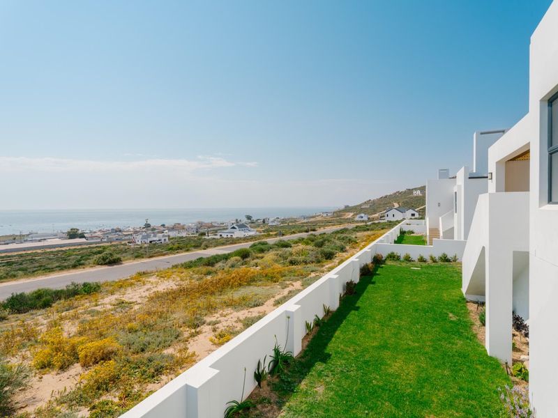 Elevated view overlooking the coastal landscape, featuring a well-maintained lawn, modern white boundary walls, and clear sightlines to the ocean.