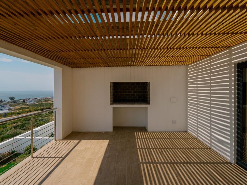 Covered balcony featuring a timber slat ceiling, built-in braai, stainless steel balustrade, and expansive coastal views.