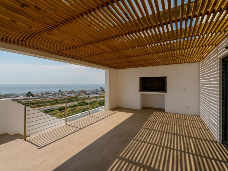 Spacious covered balcony featuring a timber pergola, built-in braai, and stainless steel balustrade, offering expansive coastal views.